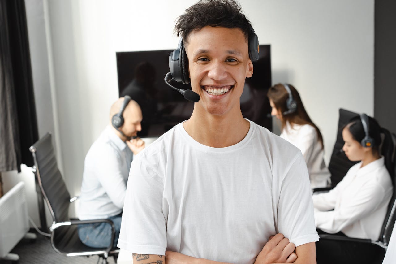 Young call center agent smiling confidently while colleagues work in the background, showcasing teamwork and customer service.
